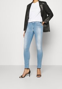 Jeans ajustados de color azul claro, hechos de denim, con un acabado deslavado y diseño de cinco bolsillos, combinados con una camiseta blanca y un blazer de cuero negro.