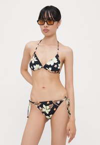 Blomstrete bikini-sett med svart bunn, med kremfargede og oransje blomster. Triangel-top med knytelist; bunnen har sidesnøring. Glatt tekstur.