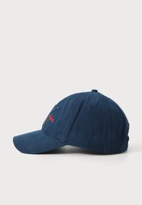 Marineblaue Baseballmütze aus Stoff mit gesticktem roten "Klein"-Logo auf der Vorderseite, mit gebogenem Schirm und Belüftungsöffnungen.