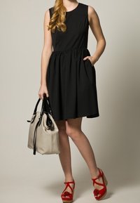 Robe noire sans manches avec une taille froncée, associée à un sac beige clair et des sandales compensées rouges avec des accents floraux.