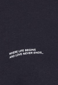 Maglietta in tessuto costellato blu navy scuro con testo ricamato bianco: "DOVE LA VITA INIZIA E L'AMORE NON FINISCE MAI_" in formato curvo.
