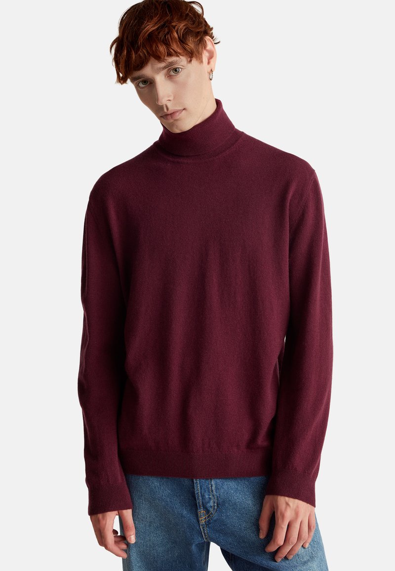 Burgundowy sweter z golfem charakteryzuje się miękką plecionką, długimi rękawami i dopasowanym krojem, zestawiony z jasnoniebieskimi dżinsami.