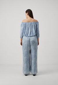 Salopetă de culoare bleu deschis, cu umeri goi, mâneci lungi, talie elastică, picioare largi și un model texturat. Țesătură fină cu o strălucire subtilă.