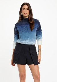 Maglione a maglia con gradiente blu, colletto alto, maniche lunghe e una consistenza morbida, abbinato a pantaloni navy con tasche a toppa.