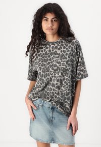 Šedé tričko s leopardím potiskem a krátkými rukávy v uvolněném střihu, spárované s modrou džínsovou mini sukní.