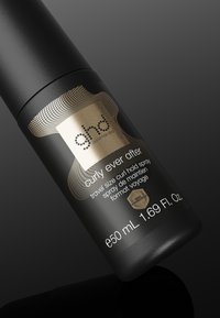 Flacon spray noir étiqueté "ghd curly ever after" taille voyage, spray fixation boucles avec protection thermique, 50 ml, sur une surface sombre réfléchissante.