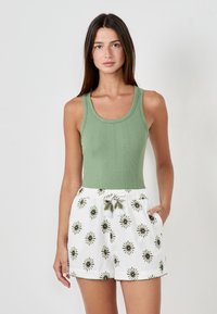 Top de tirantes verde acanalado combinado con pantalones cortos blancos que presentan bordados de flores y una cintura con cordón y borlas.