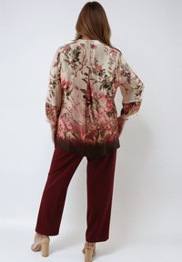 Floral-patterned blouse in cream, featuring pink and green blooms, gradates to brown. Paired with burgundy pants and beige block-heeled sandals.