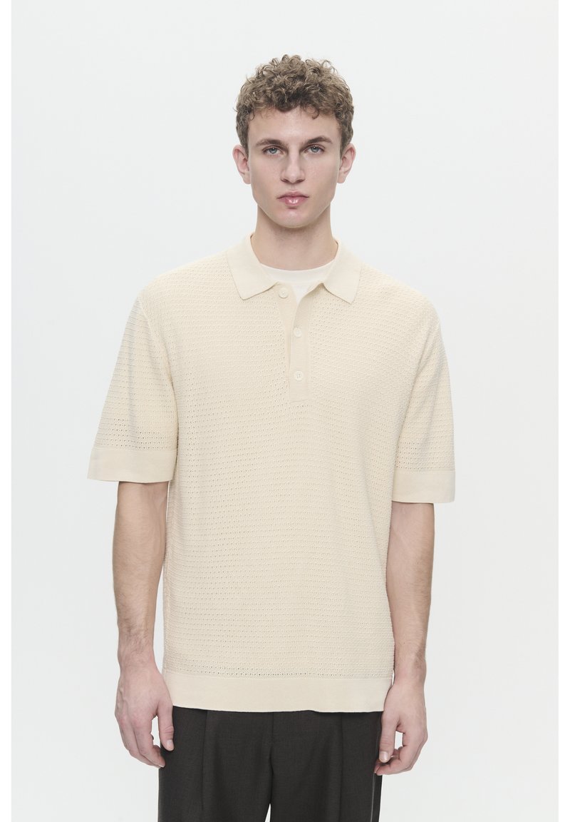 Polo shirt court beige clair à manches courtes avec un motif en maille texturé, patte de boutonnage à trois boutons et col et poignets côtelés.