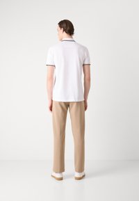Hvits polo-skjorte med svart trim, kombinert med beige bukser. Antrekket har et enkelt design og avslappet passform, sett fra bak.