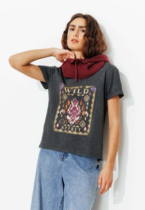 T-shirt gris à manches courtes avec un motif graphique coloré mettant en avant des flammes et des motifs floraux, associé à un col roulé en tricot bordeaux.
