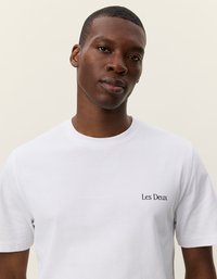 Λευκό βαμβακερό t-shirt με κοντά μανίκια, διαθέτει ένα μικρό μαύρο λογότυπο "Les Deux" στην περιοχή του αριστερού στήθους, απαλό κατά την υφή.