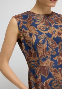 En figursydd klänning med en blå bakgrund och ett intrikat brunt blommönster. Tyget har en texturerad finish och en båturringning.