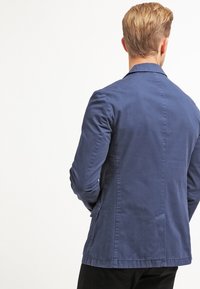 Námořnická modrá, lehká sako s hladkou texturou, s jedním zadním rozparkem a dvěma bočními kapsami, navržené pro přiléhavý siluetu.