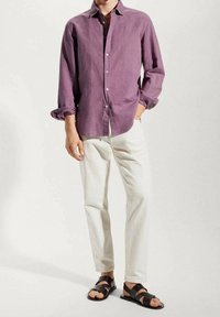 Camisa de lino morada de botones, con las mangas arremangadas, combinada con pantalones blancos y sandalias negras de múltiples correas. Diseño limpio y minimalista.