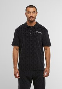 Black textured polo shirt with a collared neck, three buttons, and the "COLUCCCI" logo on the upper left chest. Soft fabric and relaxed fit.