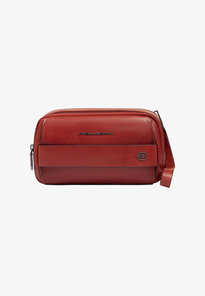 Pochette zippée en cuir rouge avec détail de sangle à l'avant et logos en métal, forme rectangulaire compacte avec boucle de transport sur le côté.