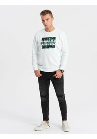 Biała bluza z grafiką z napisem "OMBRE", w połączeniu z czarnymi przetartymi dżinsami i białymi trampkami z akcentami w kolorze teal.