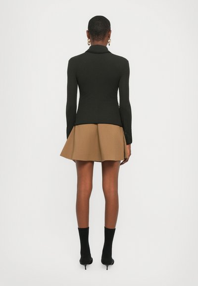 Blazer nero fitted con maniche lunghe, abbinato a una gonna a campana color beige. Il modello indossa stivali con tacco neri e calze fino al ginocchio.
