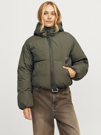 Zelena puffer jakna s kapuljačom, zatvaranjem na zip i elastičnim manžetama. Uparena s smešnim visokim farmerkama koje imaju prednju džep i pojas.