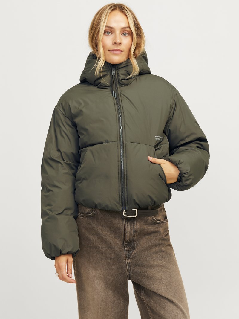 Zelena puffer jakna s kapuljačom, zatvaranjem na zip i elastičnim manžetama. Uparena s smešnim visokim farmerkama koje imaju prednju džep i pojas.