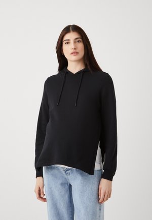 Svart hoodie med snörning, sidoflikar och långa ärmar. Matchad med ljusblå denimjeans. Slät textur, avslappnad design.