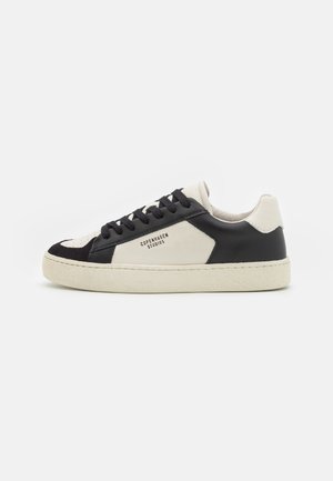 Zapatilla baja en negro y blanco con cordones negros y texto "Copenhagen Studios" en un lateral, con una suela texturizada de color crema.