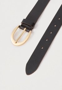 Brūns ādas jostas, kas aprīkota ar zelta toņa metāla sprādzi, ar vairākiem regulēšanas caurumiem jostā un gludu tekstūru.