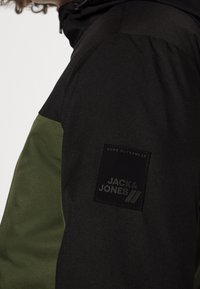 Černá a olivově zelená bunda s texturovaným povrchem, na rukávu s nášivkou s logem "JACK & JONES" a kapucí na šňůrku.