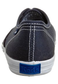 Baskets en toile marine avec semelle en caoutchouc blanc, présentant un design cousu, un écusson logo à l'arrière et une pointe ronde. Style minimaliste et décontracté.