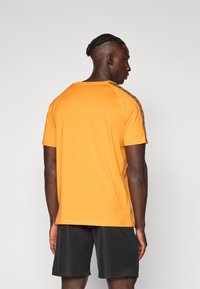Feloranje t-shirt met contrasterende geprinte schouderafwerking en korte mouwen, gecombineerd met zwarte shorts, weergegeven vanaf de achterkant.
