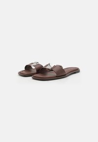 Bruna sandaler i plast har en slät syntetisk ovandel med en silverdetalj. Sulan är platt och svart, vilket ger en minimalistisk design.