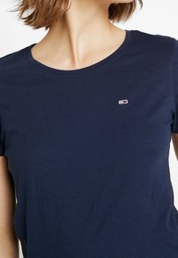 Tmavě modré bavlněné tričko s kulatým výstřihem, krátkými rukávy a malou nášivkou loga na levé hrudi. Měkká struktura, jednoduchý design.