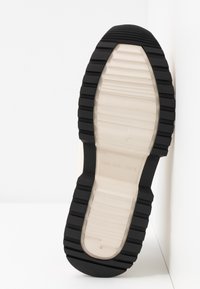 Suola della scarpa con un cuscino beige e suola in gomma nera. Presenta scanalature e una superficie liscia, offrendo aderenza e stabilità.