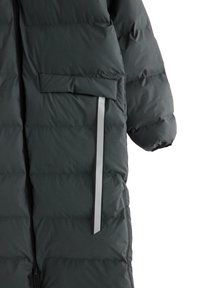 Pitkältä mustalta pehmeältä talvitakilta, jossa on läpällinen tasku ja heijastinnauha etupuolella, osittain näkyvä hiha ja etuvetoketju.