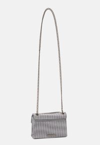 Černobílá kabelka s kostkovaným vzorem vyrobená z texturované tkaniny, s stříbrným řetízkovým popruhem a klopou se zapínáním na placku s logem.