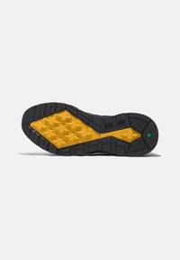 Suola delle calzature nera con un motivo testurizzato giallo. Presenta lugs di trazione multidirezionali per una migliore aderenza e un dettaglio di accento verde.