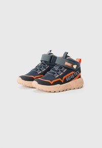 Chaussures mi-hautes noires et orange avec une étiquette GORE-TEX, présentant une sangle de sécurité, une semelle texturée et un design robuste pour une utilisation en plein air.