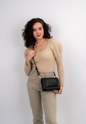 Black leather crossbody bag with gold hardware and brand logo, featuring a structured shape and adjustable strap. Model wears a beige knit top.