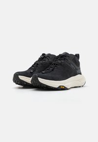 Pantofi sport din suede negru, cu o suprafață texturată, vârf rotunjit și intermediar alb în contrast. Au șireturi negre și brant Vibram pentru aderență.