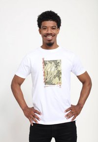 Hvid T-shirt med korte ærmer, der har et bambusprint i sort og beige med røde accenter på fronten. Glat bomuldsstof, klassisk pasform.