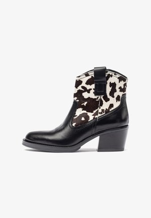 Botín de cuero negro con empeine de estampado de vaca, que presenta un tacón bajo de bloque y una lengüeta para facilitar su uso. Textura suave y diseño elegante.