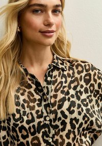 Koszula na guziki w cętki lamparta wykonana z lekkiego materiału, z kołnierzykiem i subtelnymi plisami, wyposażona w duże guziki i luźny fason.