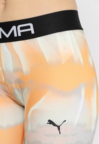 Legginsy wykonane z elastycznego materiału, z abstrakcyjnym pomarańczowo-białym wzorem, z czarnym pasem i czarnym logo Puma.