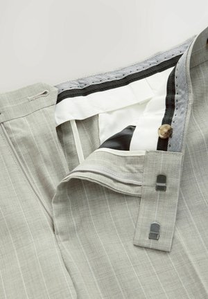 Lys grå stribede bukser med knaplukning, lynlås og tekstureret stof. Den indvendige talje har elastik og kontrasterende sort kant.