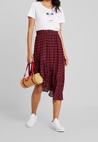 Rood en marineblauw geruite asymmetrische rok met een geraffineerde taille, gecombineerd met een wit T-shirt met een mopshondgrafiek en witte sneakers.