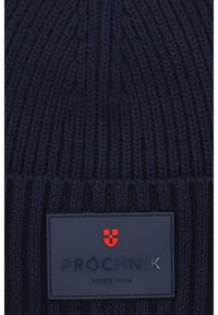 Granatowa dziana czapka z prążkowanym wzorem, z prostokątną naszywką logo w ciemnoniebieskim kolorze z czerwonymi i srebrnymi akcentami.