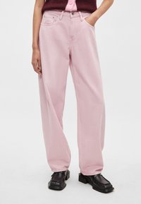 Gaiši rozā plašu bikšu džinsi no džinsa auduma ar priekšējām kabatām, jostas cilpām un izšūtiem akcentiem. Kombinēti ar melnām, masīvām zābakām.