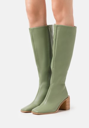 Bottes montantes en cuir vert avec un bout carré, une fermeture éclair et un talon en bois empilé. Texture lisse avec un design minimaliste.