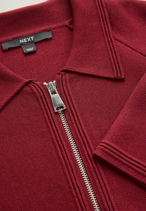Burgundská zipová bunda s polo límečkem, texturovaná tkanina, stříbrný zip a kontrastní prošití u límečku a rukávů.